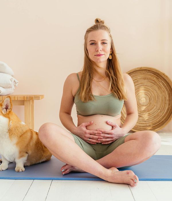 Smiling pregnant woman sitting comfortably on a yoga mat.